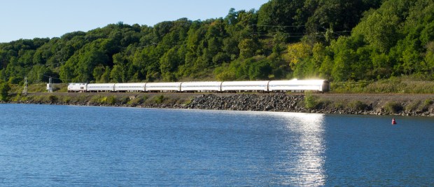 Passenger train along river with sun reflection