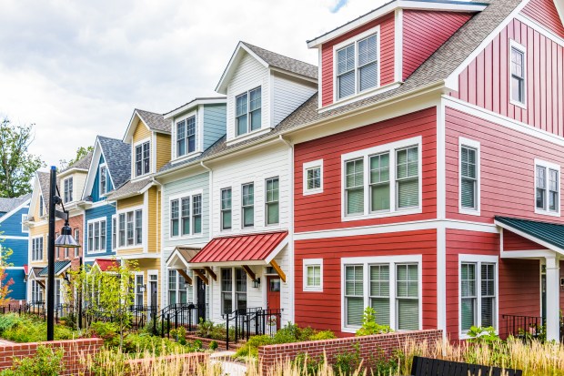 Row of colorful, red, yellow, blue, white, green painted residential townhouses, homes, houses with brick patio gardens in summer